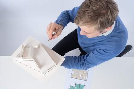 A male architect with a model of the house is photographed from above. The architect makes notes...