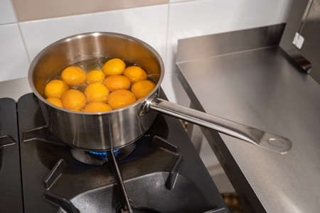 Preparation of mandarins in syrup. On the stove is a ladle of tangerines and syrup. Whole tangerines in the peel are cooked in syrup. Meals of the citrus. The dessert of citrus.の写真素材