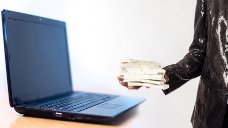 A laptop. A man in a shiny jacket with money. Man with money near the laptop. Dollars. Concept - the...