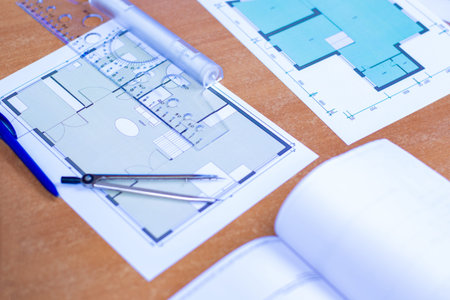 Drawings of a building on a wooden table. A ruler next to the drawings of the room. Concept -...