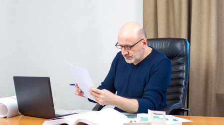 Architect works with a laptop. A man is sorting papers on the desktop. Man with drawings of...