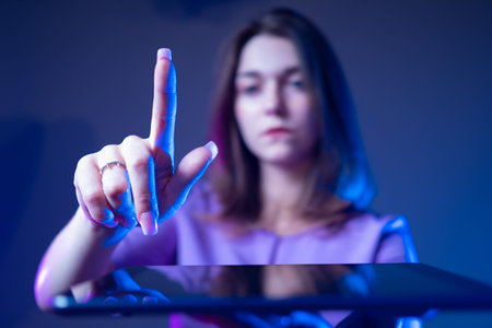 Woman with a tablet. Girl shows a finger. Studenka shows a hand gesture. Student wants to click on the tablet. Young woman on a dark background. Concept - Using Gadgets. Concept - study with a tabletの写真素材