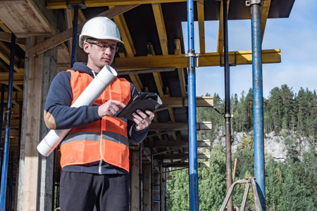 Builder with a tablet and drawings in hands. Builder the background of a house under construction....