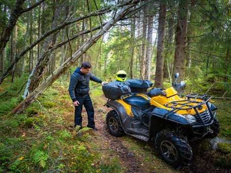 Yellow ATV in the forest. A man examines an ATV. Concept - breakdown in the middle of the forest....