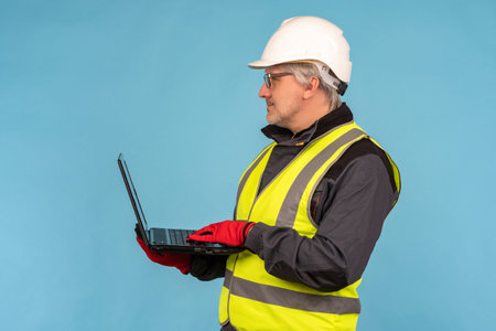 Civil engineer with a laptop in his hands. A man in an orange vest and hard hat. An architect with a...