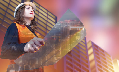 Girl architect on the background of three-dimensional models of multi-storey buildings. Woman in construction helmet with construction drawings. 3D buildings and a civil engineer.の写真素材