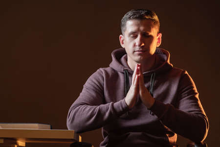 A person prays. Person is sitting with his eyes closed and his hands folded in prayer. The man prays. The guy reads a prayer, crossing his palms in front of him. A praying man on a brown background.の写真素材