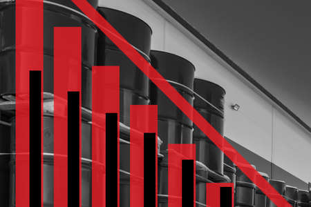 Barrels of oil are standing against the wall. Graph shows a steady decrease. Red chart. Cost of oil has been reduced. Concept is a decrease in production rates. Decrease in oil reserves in the stateの写真素材