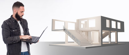 House project. Bearded architect with laptop. A man with a laptop next to a house mock-up. Architect...