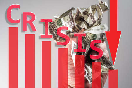 Crumpled dollars on a light background. Inscription crisis next to the falling chart. Red down arrow as a symbol of recession. Concept - Crisis in United States Economy. American dollars. Recessionの写真素材
