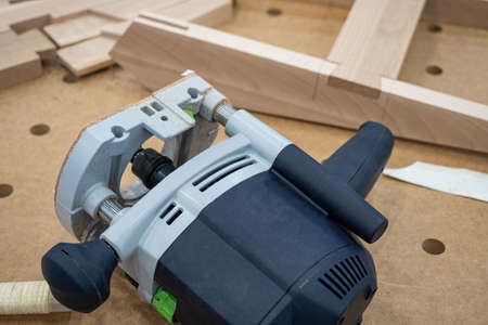 Electric cutter on a wood table. Cutter for creating grooves in wood. Portable woodworking cutter. Wood milling. Creating grooves and grooves in boards. Concept - equipment for furniture productionの写真素材