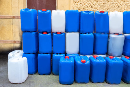 White and blue water-cans stand on top of each other. Lots plastic cans on background on wall....