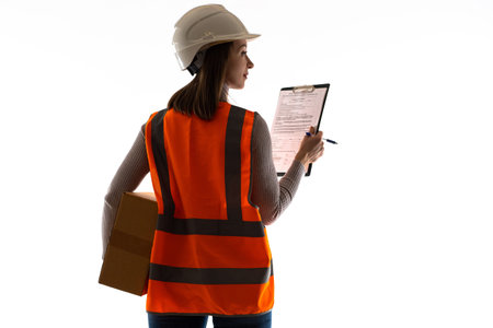 Woman with a cardboard box and a bill of lading. Female storekeeper wearing a hard hat and an orange...
