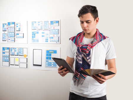 UX dessinger with a tablet in hand. He holds a palette of colors his hands. Man designer chooses a...