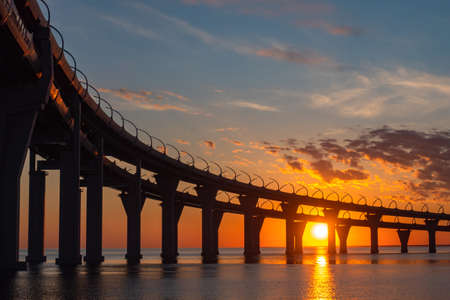 Double bridge over bay. A bridge on high supports on background sky. Sunset over bridge. Concept - road architecture. Expressways on bridges. Automotive bridgework on large columns.の写真素材