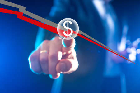 Man shows a falling graph. Concept of falling quotations in investments. Chart shows fall in financial market. Investor shows his hand to dollar icon. Investment crisis. Investor hand close up.の写真素材
