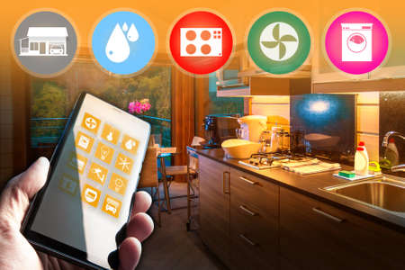 Smart home application in a smartphone. Person controls household appliances through a phone. Kitchen interior in background. Application for smart home system. App control home appliances via wifiの写真素材
