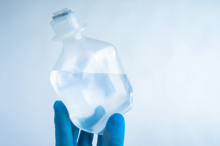 Transparent container for saline solution. Transparent medical bottle in doctor hand. Doctor hand in...