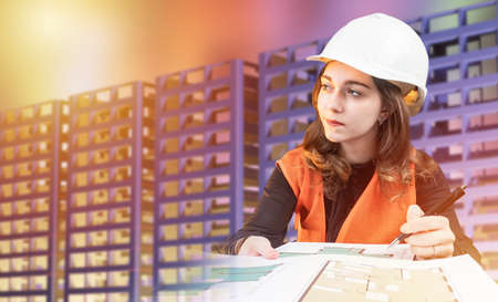 Woman in form of a builder on background of a multi-storey building. Unfinished house next to architect. Woman architect draws architectural drawings. Creating a room plan for apartment.の写真素材