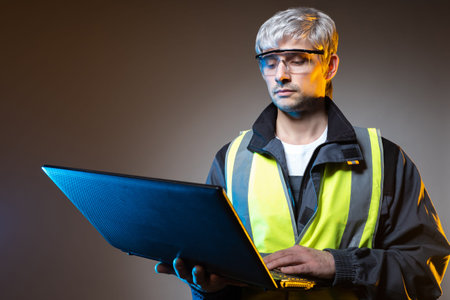 System administrator in a yellow vest. Man in work uniform with a laptop. Gray-haired system...