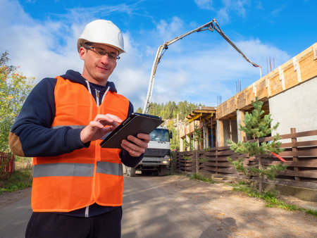 Man construction worker smiles while working. He looks at tablet computer. Builder next to a...