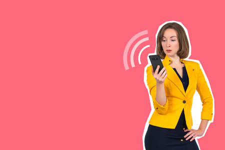 A girl with a smartphone. The woman looks at the screen of the ringing phone. A collage in the magazine style. A woman with a smartphone on a pink background. Place for the text.の写真素材