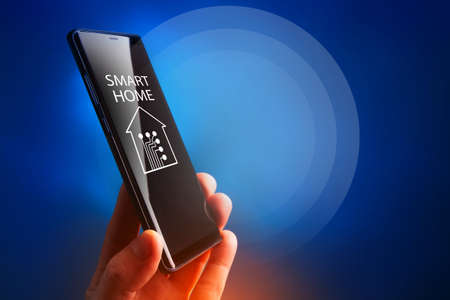Smart home technology. Hand of man with smartphone. Smart home technology control phone. IOT system control via telephone. Concept smart home technology control applications. Hand on blue backgroundの写真素材