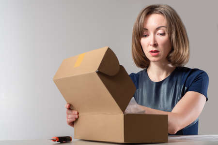 Woman owner business while working. Girl next to an open carton box. Small business owner is packing something. She prepares goods for shipment. Portrait of a businesswoman on a gray backgroundの写真素材