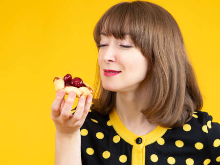 Woman eats cakes with berries. She bites cookie with delight. Girl holds a cake near her face. Young woman with a dissert in her hands. Concept - sale of dissertations. Dissert shop.の写真素材