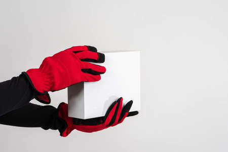 Box in courier hands. Delivery concept. Courier hands in work gloves close up. Delivery of goods by courier service. Unlabeled box on white background. Place for text. Delivery from online storeの写真素材