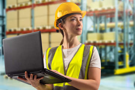 A female storekeeper with a laptop. A girl on the background of the warehouse shelves. Warehouse storage. Warehouse accounting. Organization of storage of goods. Inventory of the storehouse.の写真素材