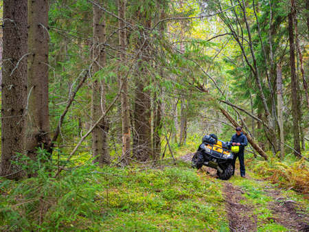 Man puts on a protective helmet. Driver next to ATV. Biker took off his helmet in forest. Drove off-road motorcycle in forest. Concept he is into extreme sports. Participation in ATV motocross.の写真素材