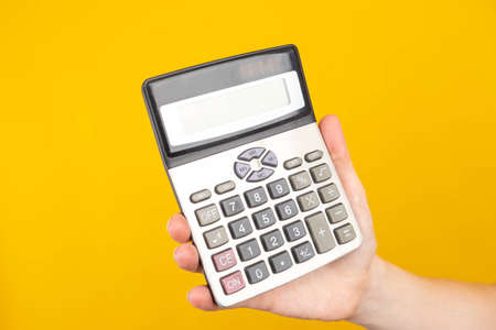 Calculator close-up. A hand with a calculator. Calculations, budgeting. Calculator as a symbol of financial calculations. Lending, calculation of the loan cost. Orange background with place for text.の写真素材