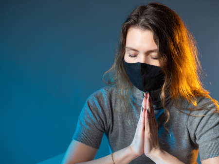 Catholic woman folded her palms. Girl in medical mask praying. Protective mask as a symbol of illness. Concept - virus infected turns to God. Sick virus  praying. Prayer to be cured of virusの写真素材