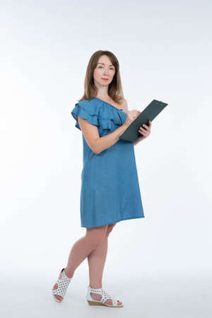 Girl with a paper tablet. Portrait of the business woman with folder. Woman makes notes in a notebook. Person with paper tablet on a light background. Woman stands and looks at the camera.の写真素材