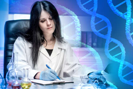 A female geneticist writes a medical report. A doctor in a white coat against the background of a DNA chain. Study of the human genome. Genetic engineering. A Biotechnological concept.の写真素材