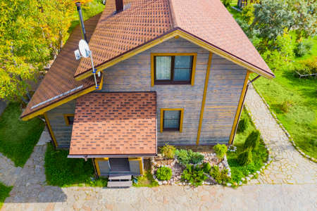 The house with a soft roof top view. Two-storey wooden cottage. A house with a TV antenna on the roof. Construction of houses. Landscape design. Stone paths and lawns around the house.の写真素材