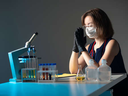Woman laboratory assistant praying. Concept she a vaccine developer. Vaccine developer pray while you work. She asks god for help in vaccine development. Microscope and test tubes near praying personの写真素材