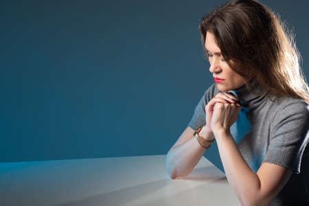 Catholic woman praying to god. She crossed her fingers and closed her eyes. Girl reads a prayer while sitting at the table. A Catholic woman performs a religious ceremony. Christian praying to godの写真素材