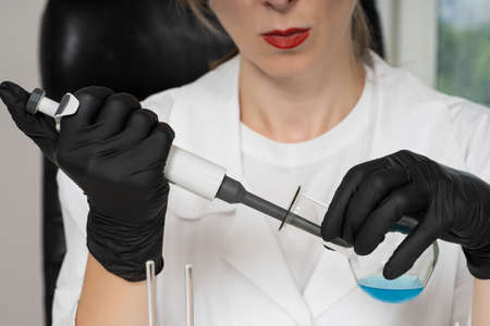 Scientist with dropper works in laboratory. Chemical tests. Medical tests. Laboratory assistant with a pipette and a flask. Female laboratory assistant collects blue chemical substance from test tubeの写真素材