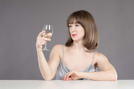Woman is drinking light wine. Concept she drinks because of personal problems. Wine in her hands symbolizes woman alcoholism. Treatment of female alcoholism. Girl with wine glass on a gray backgroundの写真素材