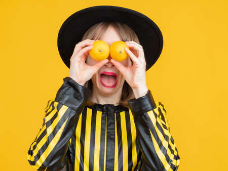 Woman with lemons in her hands. She plays fool by putting lemons to her eyes. Young girl have fun. Girl with lemons on face smiles. Concept - sale of citrus fruits. Fresh fruit saleの写真素材