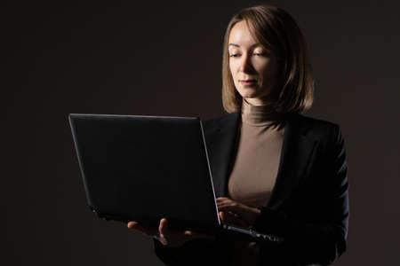 Woman with a laptop in her hands. Portrait of a businesswoman with a laptop. Adult girl on a dark background. Concept - she uses a computer to work. Businesswoman works on the Internet.の写真素材
