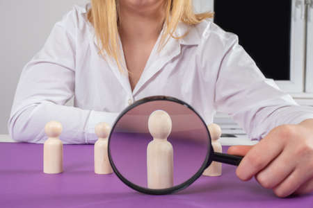 Checking employee in personnel department. Concept of checking a candidate for a vacant position. Personnel department employee with magnifying glass. Magnifier is aimed at white employee figurineの写真素材