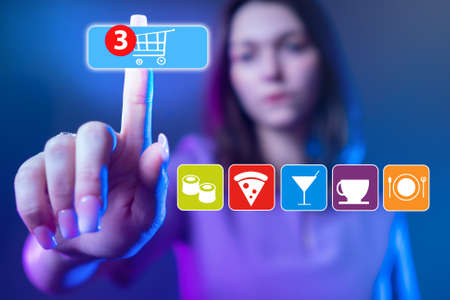 Girl orders food from restaurant. She clicks on shopping cart icon. Concept - ordering food delivery via Internet. Buying products online. Blurred girl reaches for the screen. Food delivery serviceの写真素材
