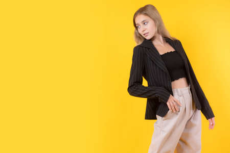 Girl on an orange background. The slender girl is arched and looks back. A long-haired young blonde. A woman in a black jacket and top. A girl with an open stomach. Place for text.の写真素材