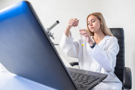 ï¿½hemist girl on the background of a laptop. ï¿½hemistry student makes laboratory work. The study of chemistry. Laboratory work in chemistry. A girl with a test tube, a microscope and a laptop.の写真素材