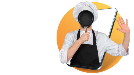 A male chef covers his face with a frying pan. The chef is joking on the smartphone screen. Culinary humor. Cooking online. Cooking according to the online course. A mobile app for teaching cooking.の写真素材
