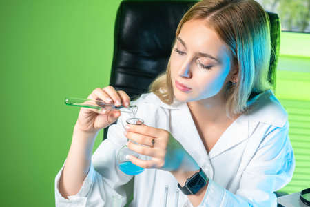 Chemistry blog. A young chemistry teacher demonstrates experiments. The girl mixes chemicals. A girl in a white coat with test tubes in her hands. She runs a blog on chemistry.の写真素材