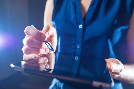 An unrecognizable woman with a tablet and a stylus. A woman uses an electronic tablet. A businesswoman using a digital pen to write on the touch panel. Electronic gadgets.の写真素材